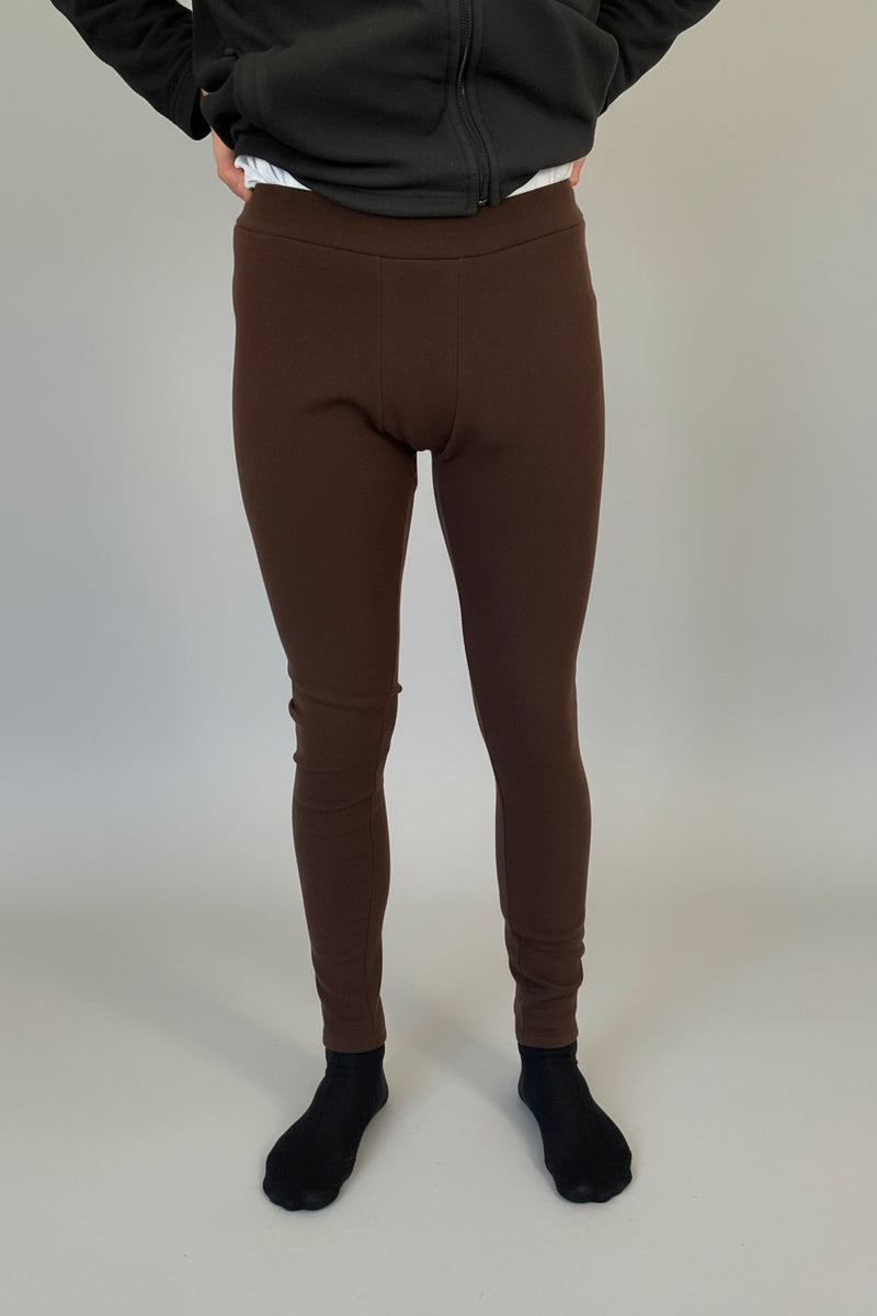 Person wearing brown leggings standing in a room with a Christmas tree and rug.