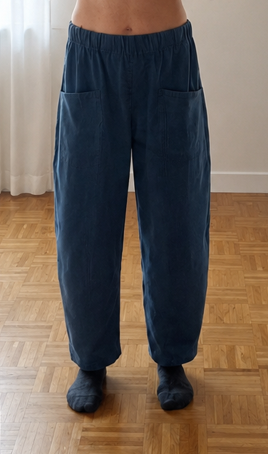 A person taking a mirror selfie in a room, wearing a bright orange cropped short-sleeve top and loose dark blue wide-leg pants.